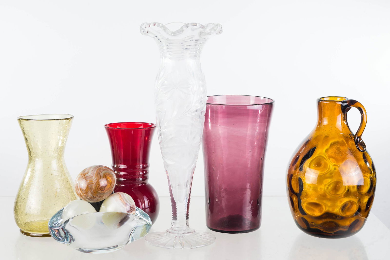 Colorful Glass Vases: Lot includes cut glass vase (12.5"H), amber glass water pitcher (hand blown), hand blown amethyst vase, crackle vase, and a ruby vase. Lot also includes a Danish style crystal ashtray and 4 stone eggs