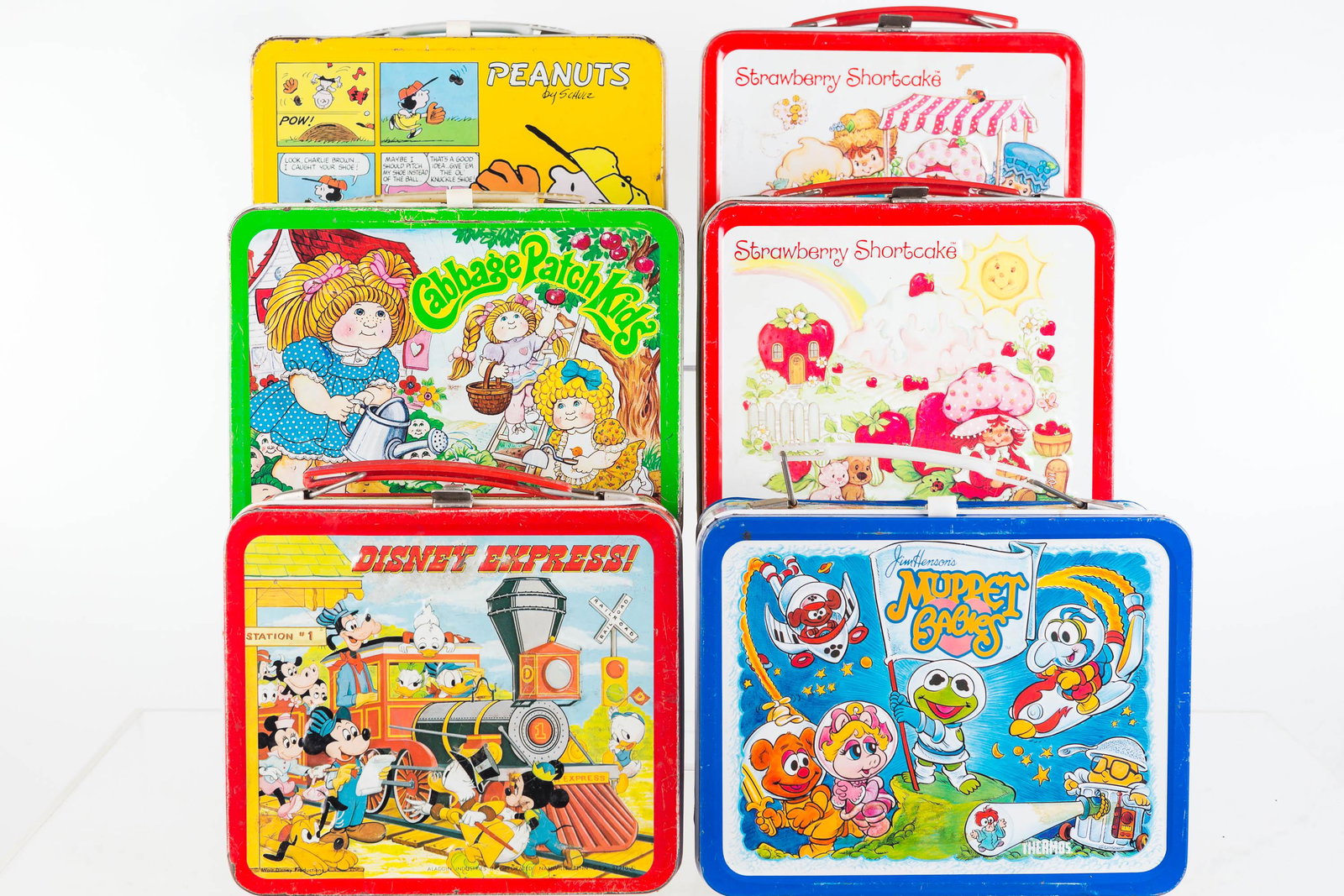 Vintage Tin Lunch Boxes Including Peanuts: Lot includes Peanuts lunch box (1965), Cabbage Patch Kids (1983), 2 Strawberry Shortcake (1980, 1981, one with thermos), Muppet Babies, and Disney Express. All show common wear.