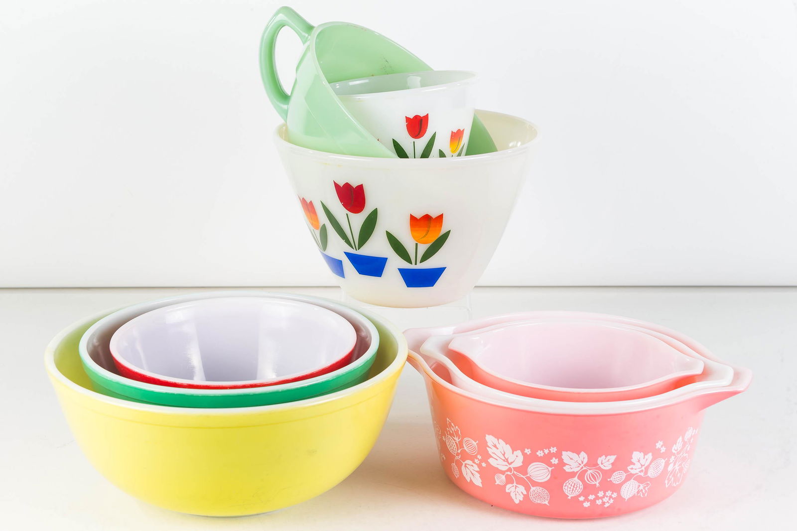 Collection of 1950s Pyrex and Fire King: Lot includes a nest of 3 floral Pyrex bowls, 2 tulips Fire King bowls, a nest of 3 colored Pyrex bowls (some wear), and a Fire King jadeite pitcher with small chip to spout.