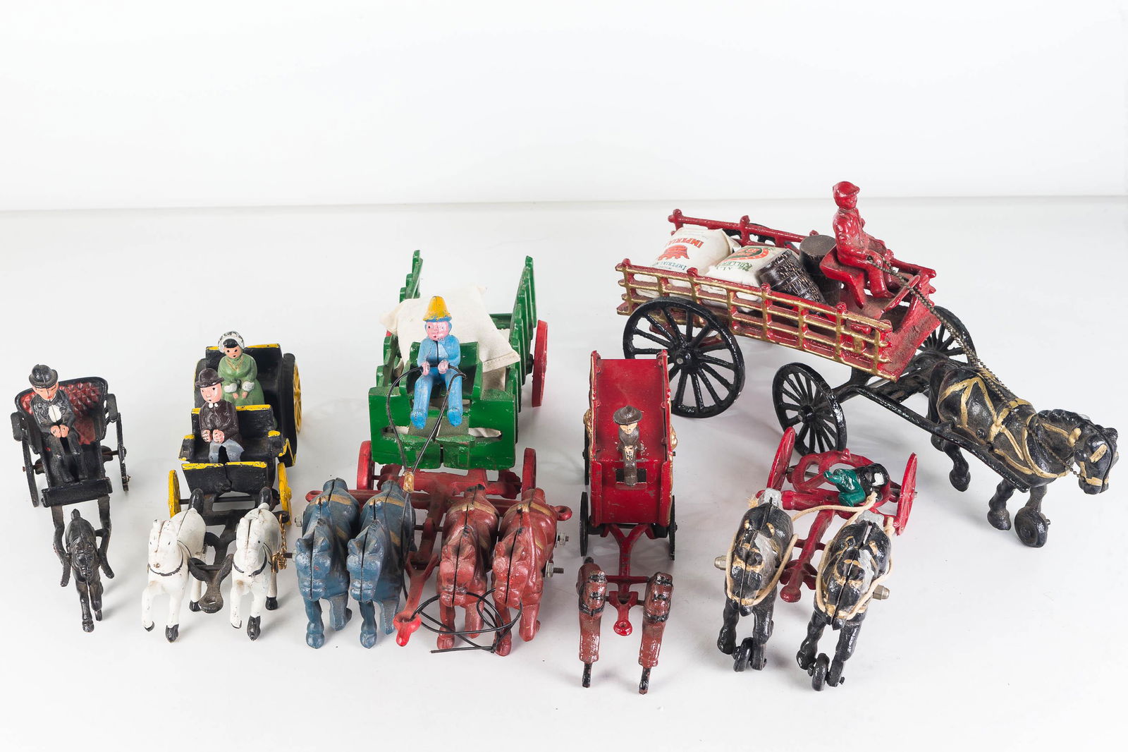 20th C Cast Iron Horse and Wagon Toys: Largest approximately 16"L. Single horse drawn wagon with contents. Lot also includes green wagon with two metal riders, a small cast and tin circus cart, a single horse and rider, and three incomplet