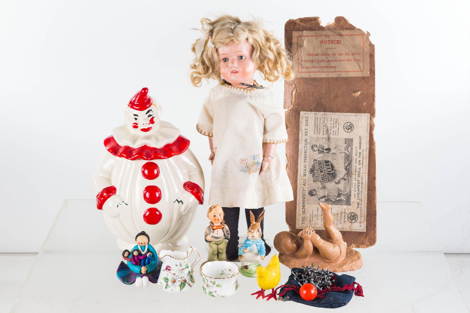 Schoenhut Doll, Hummel, and Other Figures: Lot includes a Schoenhut jointed wooden doll (15"H), with small flake on chin. Doll comes with box top (1911). Lot also includes a Hummel, a Beatrix Potter Peter Rabbit, a clown cookie jar (ca. 1950s)