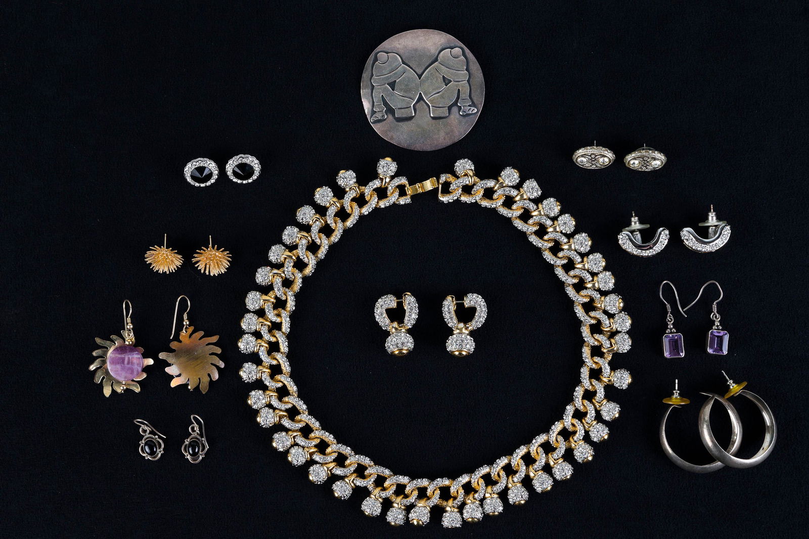 Taxco Sterling Brooch and Costume Jewelry: Lot includes Taxco sterling brooch (2.25" diameter), a pair of sterling and onyx earrings, a pair of Trifari post earrings with black central stones, a gold tone and rhinestone necklace and earrings s