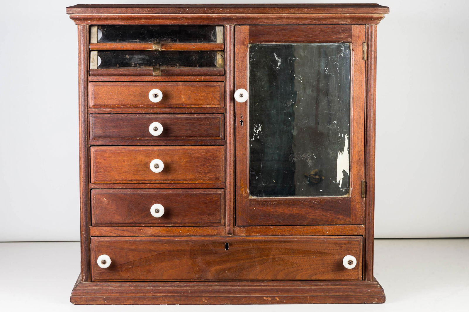 General Store Spool Cabinet, 19th/Early 20th C: Item measures approximately 22.5"H x 23.5"W x 15.5"D. Walnut construction with two glass face spool drawers above four cubby drawers and a large drawer at base. Item has one door on the right side wit