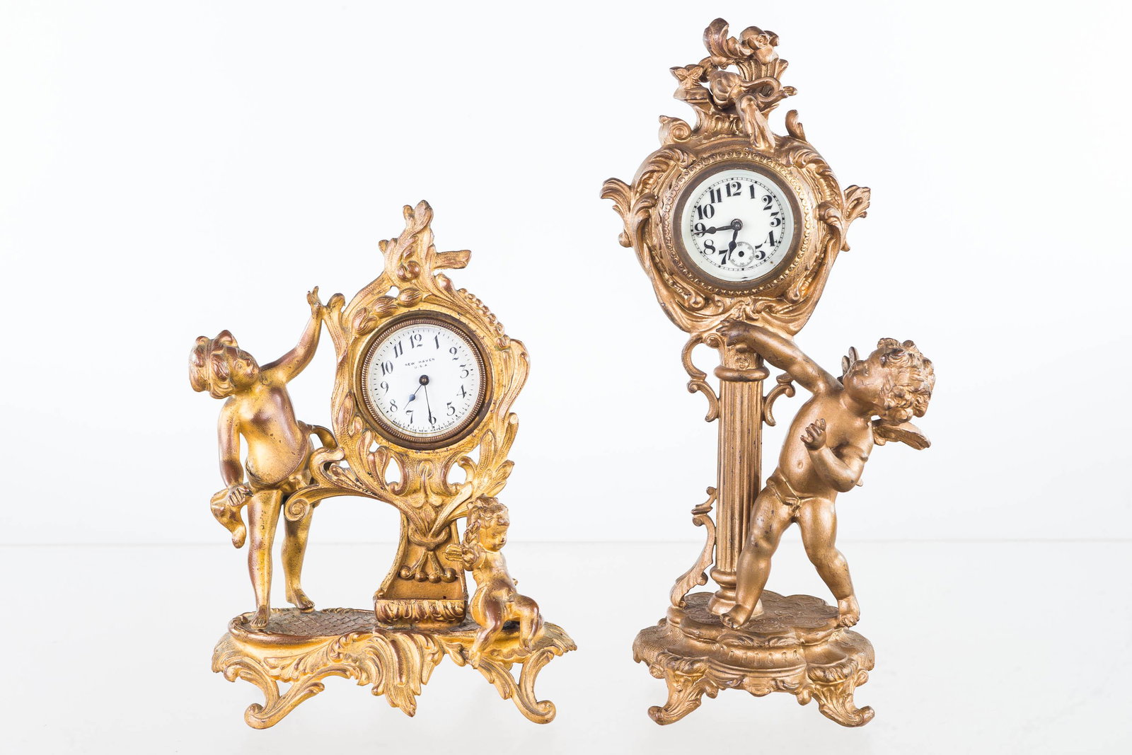 Victorian Figural Putti Clocks (2): Larger measures approximately 11.5"H. Porcelain face missing second hand. No company name was found, but 1894 Pat. date present. Second clock is a New Haven clock with a child and a putti figure. Cloc