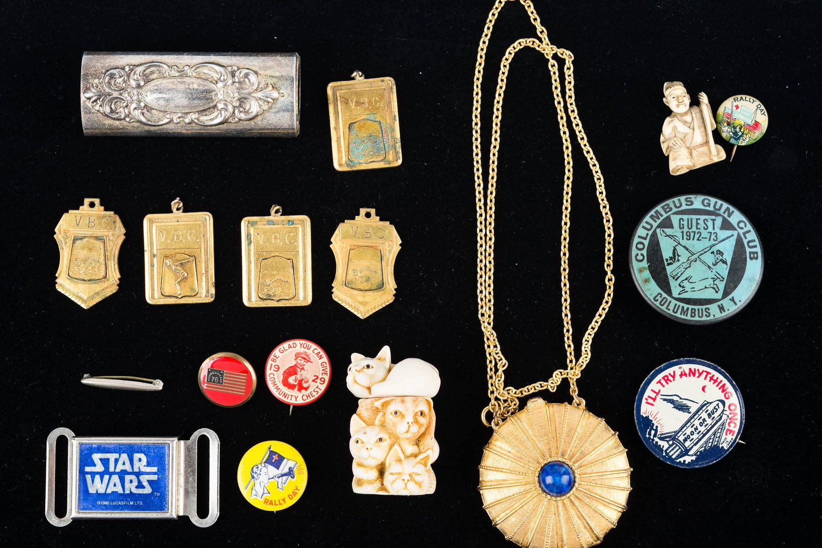 Eclectic Collection: Lot includes two carved Netsuke style items, 1980 Star Wars belt buckle, vintage Estee Lauder perfume, compact necklace, early swimming and sport medals, pin backs, and guest hunting pass.