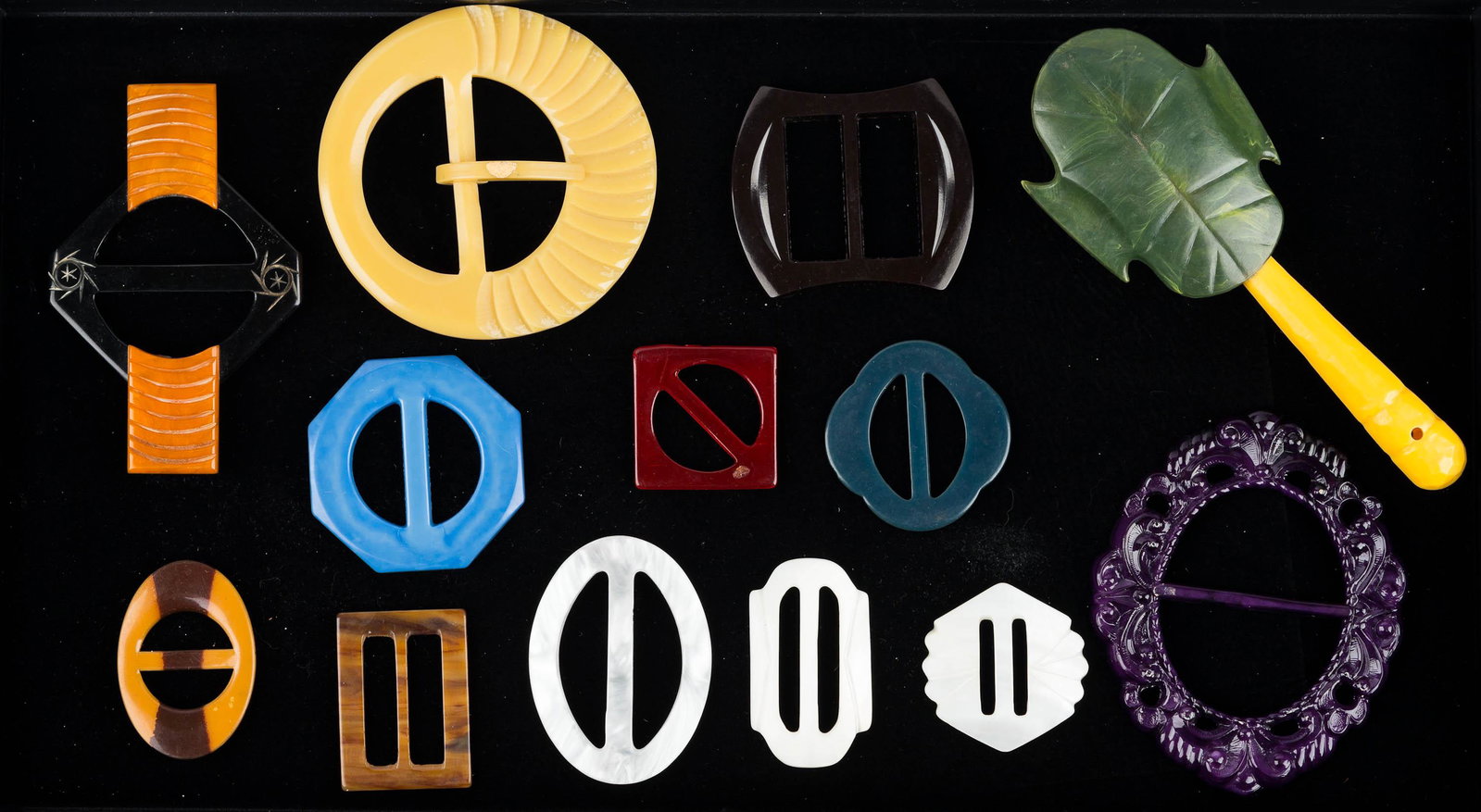Estate Bakelite Buckles and Celluloid Rattle: Lot includes three bakelite buckles to include Art Deco design butterscotch and black bakelite, square black and small stripe bakelite, other buckles including mother of pearl and colorful plastics, a