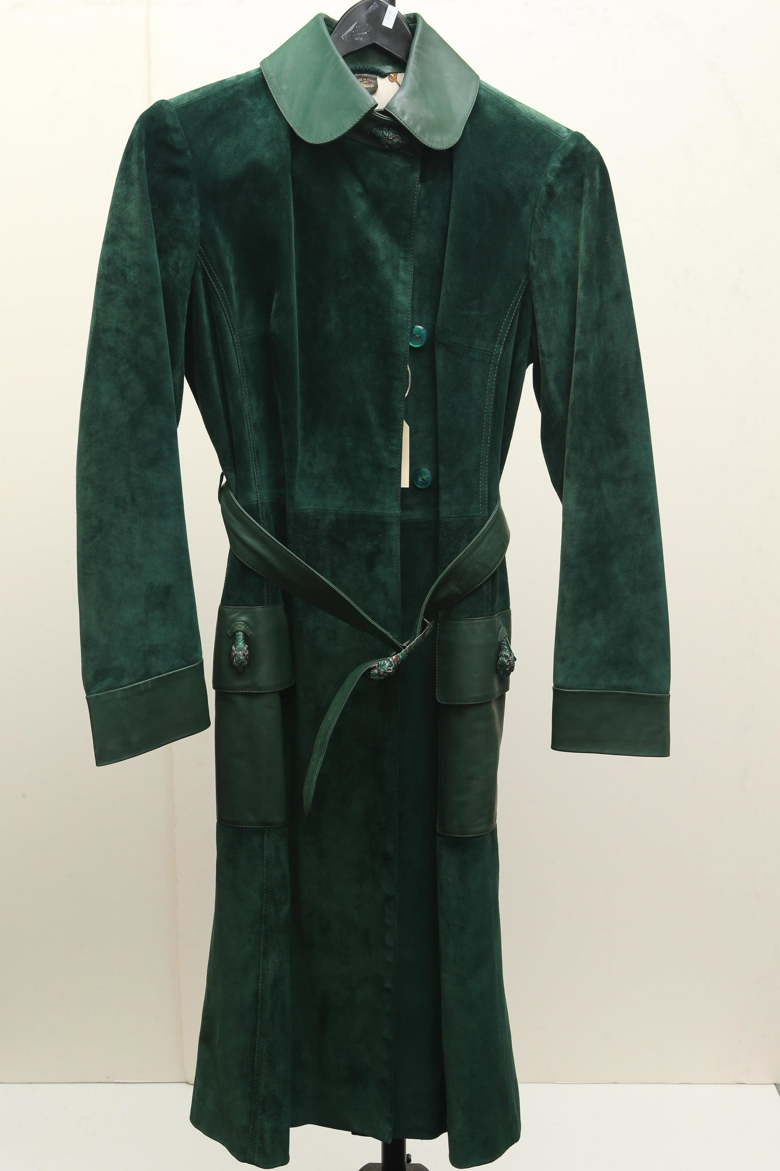 Gucci Green Suede Coat: Gucci knee length, hidden front button down coat in green suede with leather collar, cuffs, patch pockets with flaps, and belt. Belt sports a double headed metal with green enamel tiger buckle. Metal 