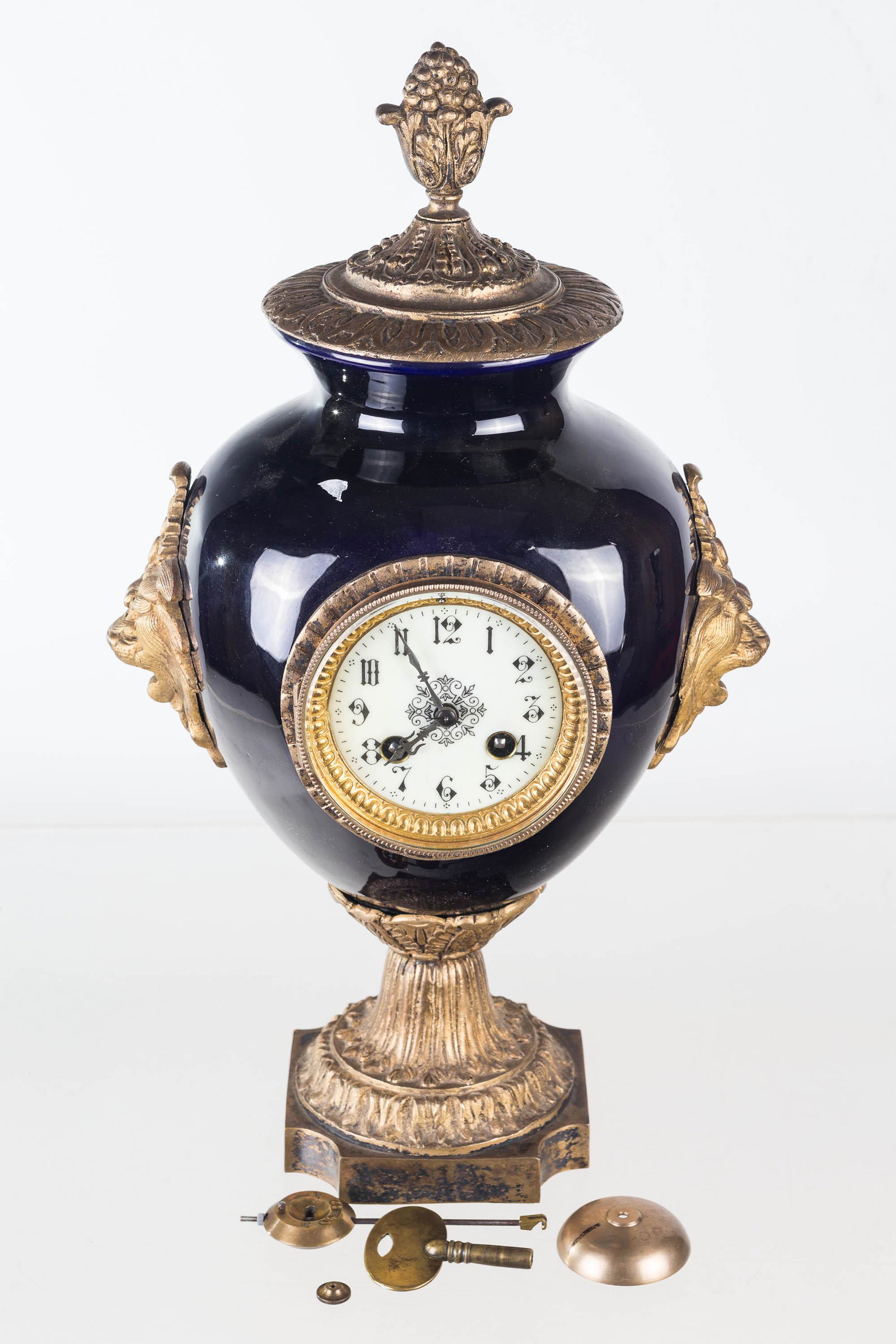 Vintage French Porcelain and Brass Mantel Clock: This clock measures approximately 18"H and has a blue/black porcelain body, decorative porcelain face, brass base, finial, and lion's head handles. Interior of clock is marked with a horseshoe shape s
