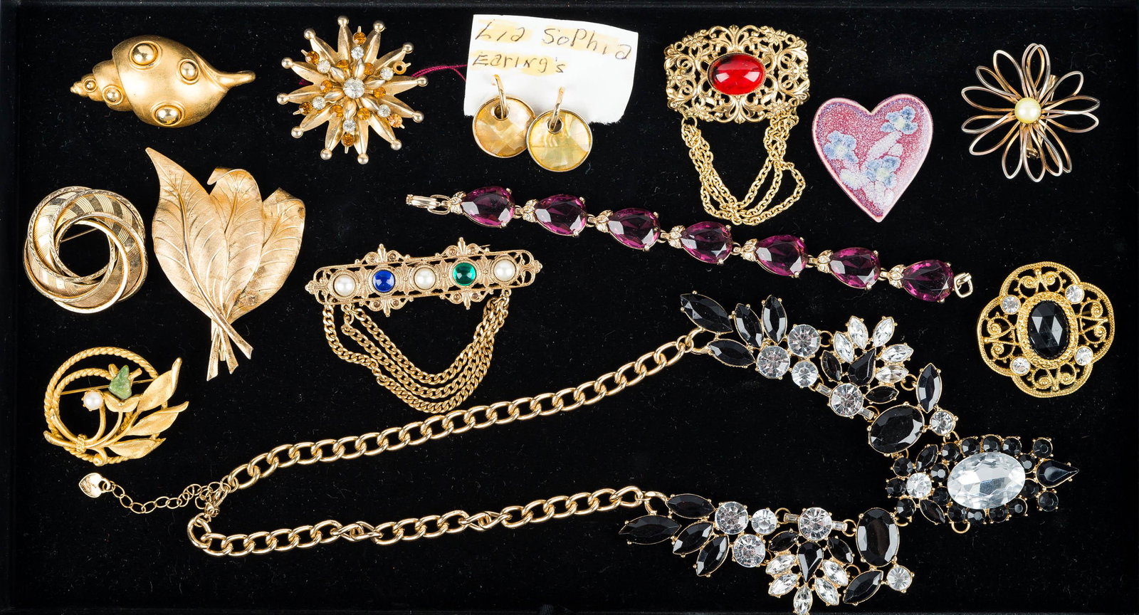 Rhinestone and Gold Tone Jewelry Grouping: a large black and clear rhinestone necklace marked JM, bracelet with purple rhinestones, Lea Sofia enameled post earrings, conch shell brooch, and other jewelry with colorful stones.
