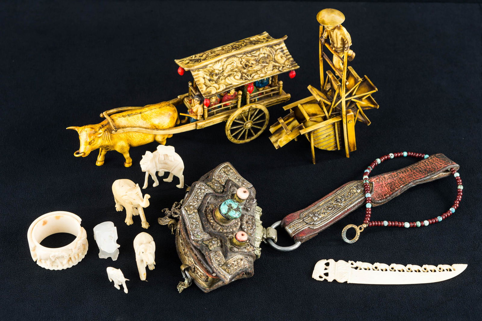 Asian Carved and Celluloid Figures: celluloid man and water wheel, and celluloid ox cart with figures, carved elephants, a camel, and a napkin ring. Lot also includes an ornate change purse in as-found condition.