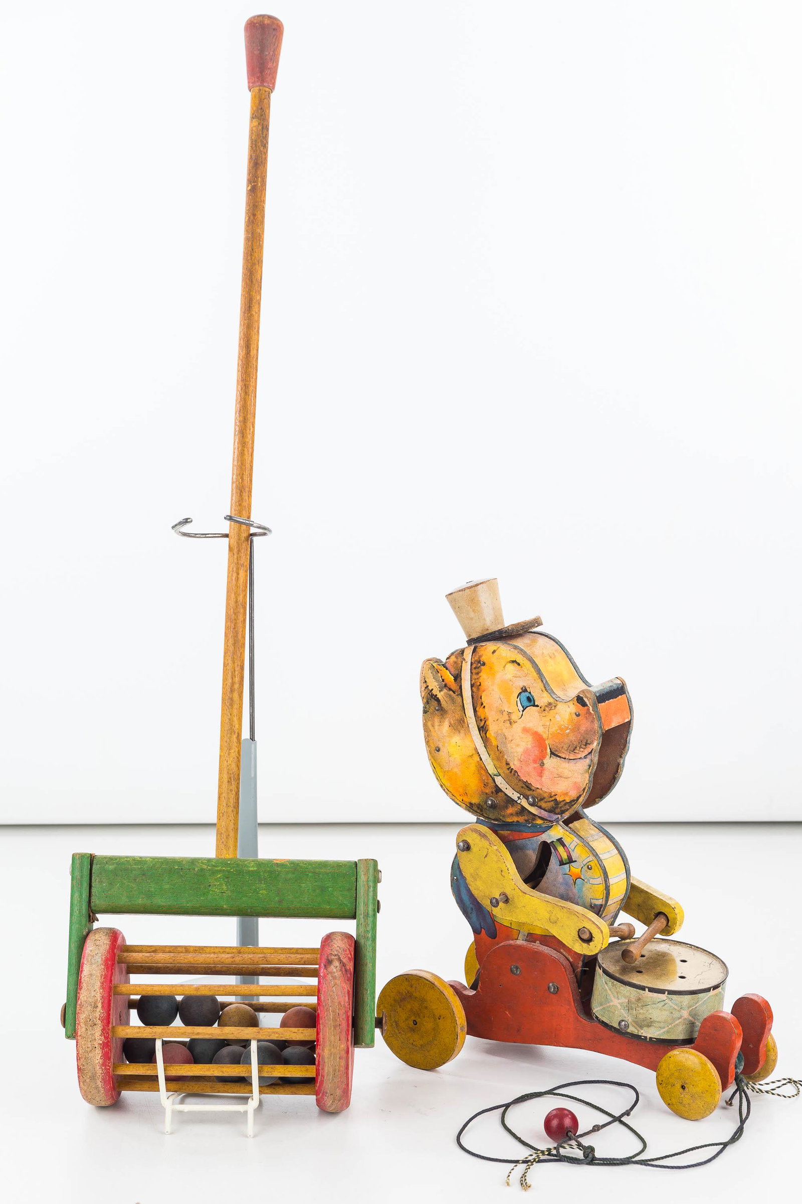 Vintage Toy Duo: Lot includes rolling lawnmower toy (26"L), constructed of wood with balls in roller, and a vintage Fisher Price No 102 pull toy bear, functional, with drum. Graphics show common wear.
