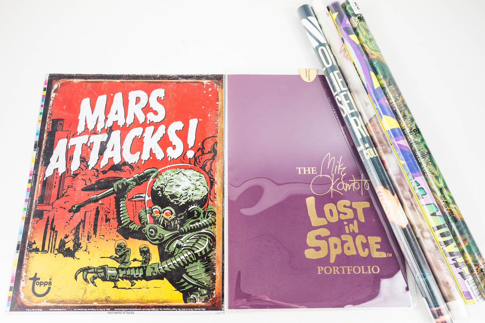 Mars Attacks and Lost In Space Posters: The Mike Okamoto 1991 Lost in Space Portfolio with 7 prints; a Lost in Space poster #1 The Innocents, a Mars Attacks metal promo sign by Topps c2012; and 2 other rolled Mars Attacks movie posters and
