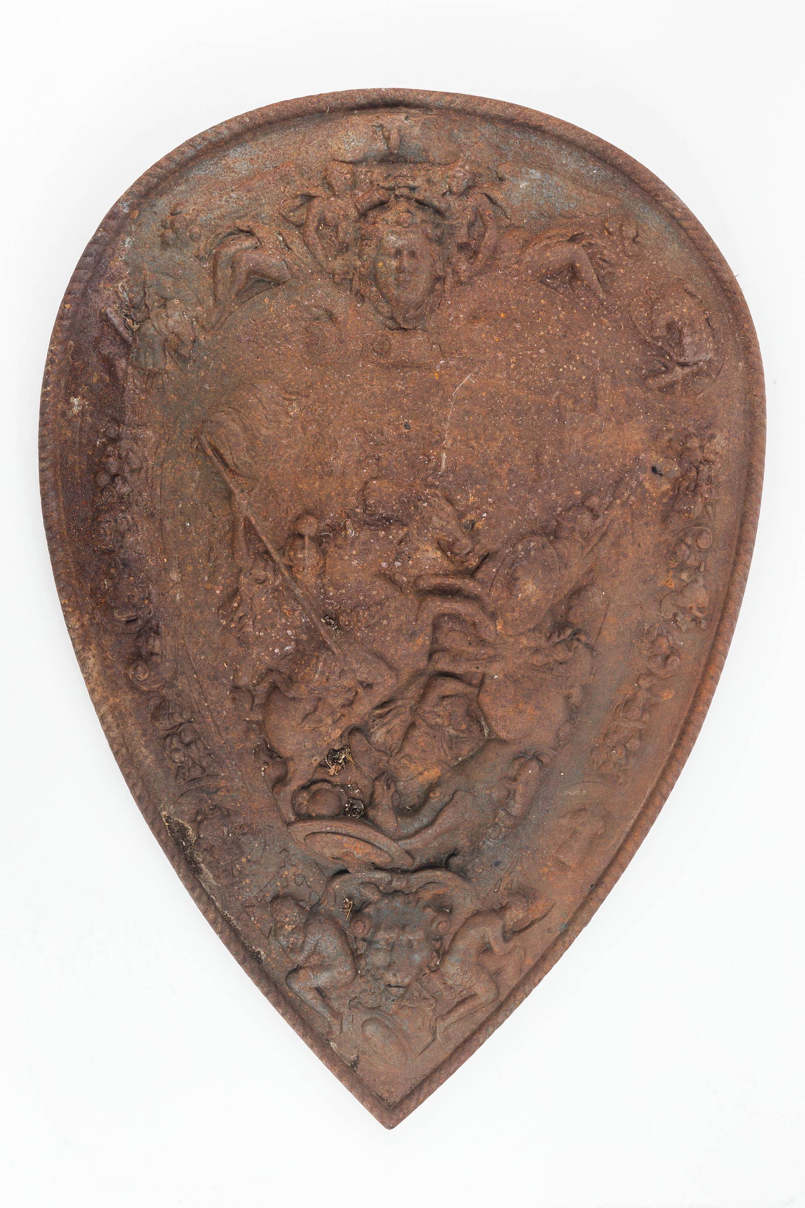 Decorative Cast Iron Shield: This shield depicting an ancient battle scene is made from a single piece of cast iron and measures approx. 24" H x 17" W. It has an obscure company marking on back, and item is oxidized.