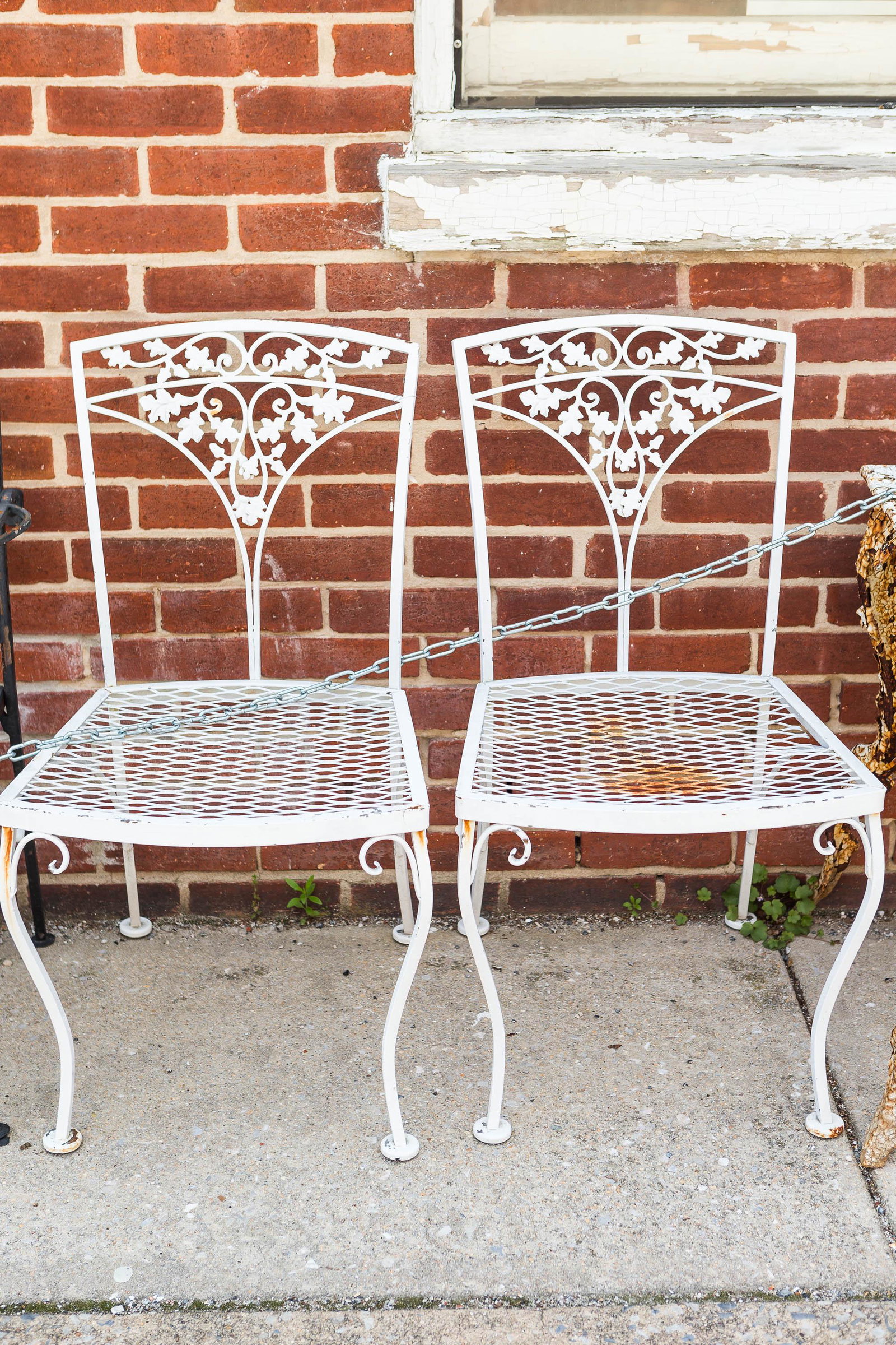 White Metal Patio Chairs (Pair): This pair of patio chairs features an oak leaf motif on the backs; one seat needs minor repair.
