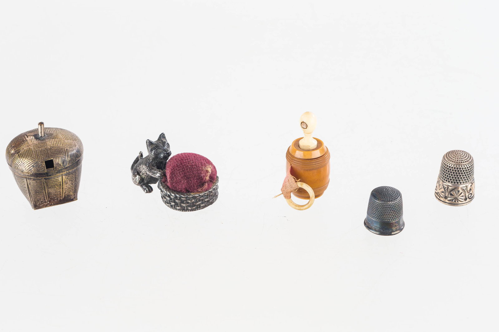 Antique Sewing Miniatures: This lot of sewing items includes a sterling silver unmarked cat pincushion, (2) sterling silver Victorian thimbles, a carved barrel measurer, and a miniature silver type basket with hand-blown glass 