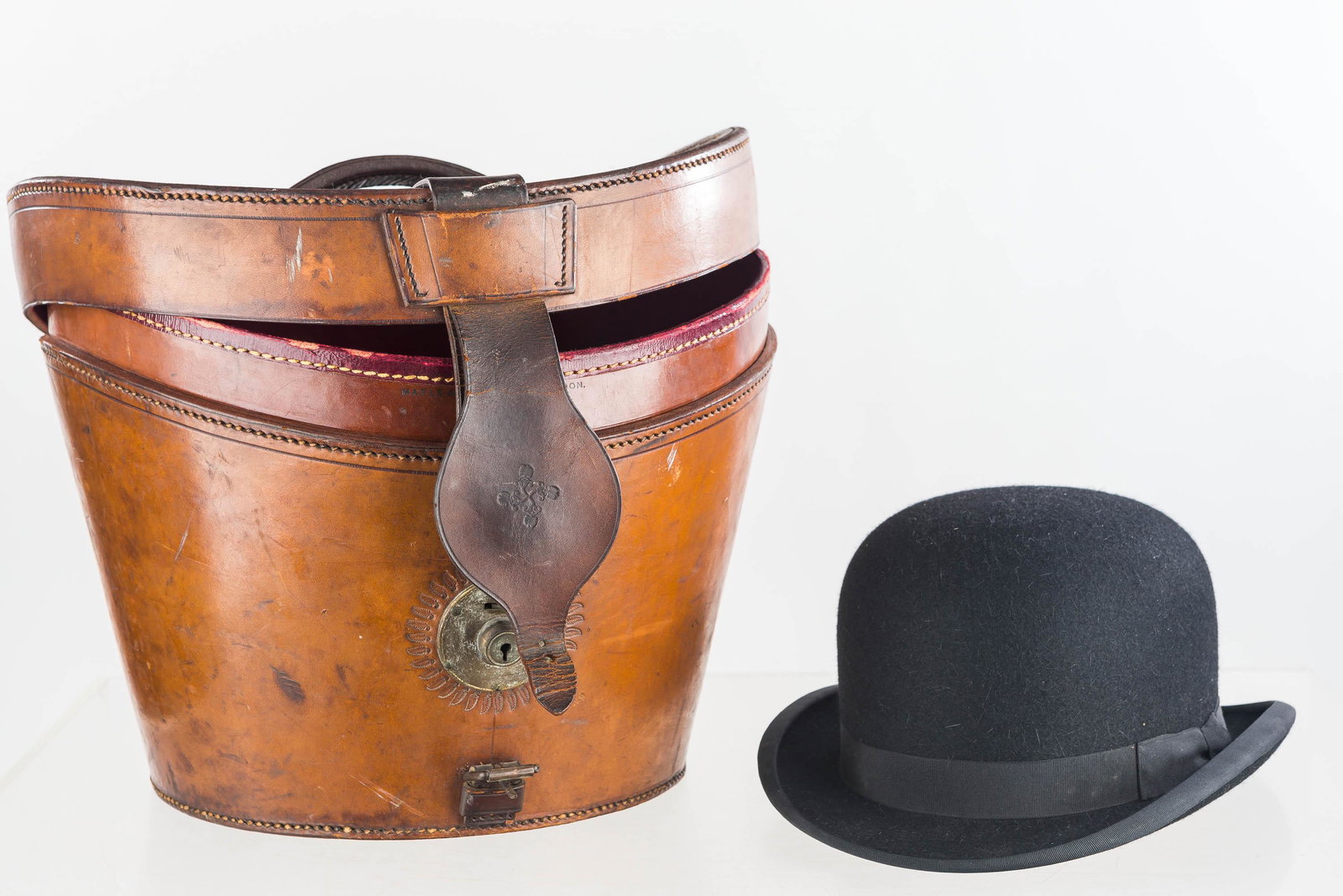 Antique Leather Travel Hat Case and Hat: This antique, leather, hand-stitched, early, Victorian hat travel case has embossed detail around brass lock, and leather carrying handle lined in quilted red silk. It is signed "London, Maple, and Co