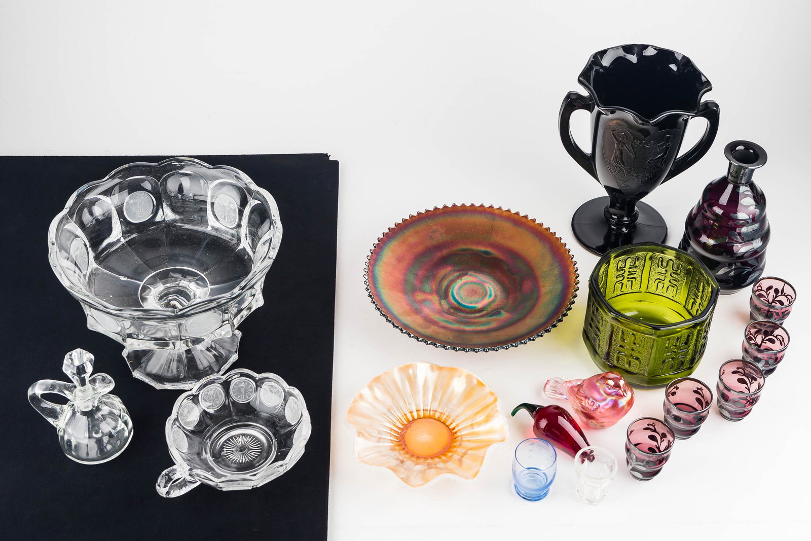 Colorful Glassware Grouping: Grouping includes an amethyst glass vase with two figures on the side measuring approx. 8" H, a pink Fenton bird, a purple carnival glass candy dish, an opalescent Fenton-type dish, a coin print compo