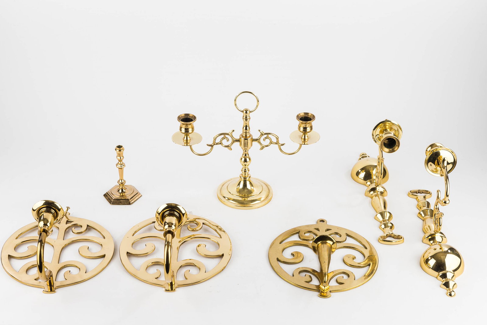 Baldwin & Other Brass Candlesticks: The Baldwin double-arm candelabra measures approx. 9" H. Also includes a Williamsburg miniature candlestick, a pair of quality brass wall sconces with cannonball base, and (3) trivet style wall sconce