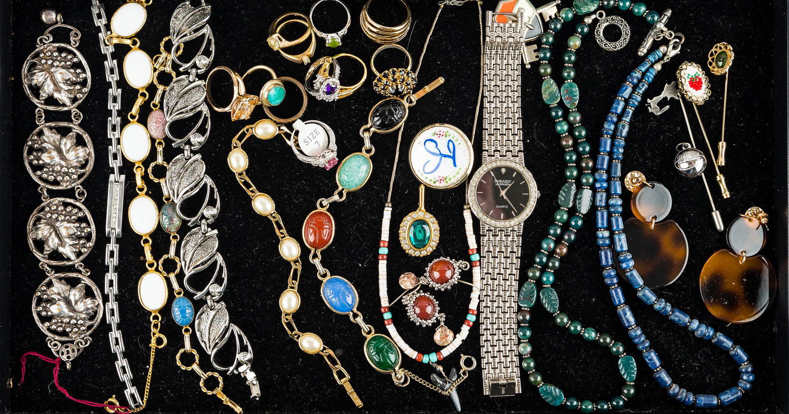 Decorative Rings & Costume Jewelry: There are (11) rings, some with rhinestones, ranging from size 5 to size 8; an Embassy Gruen ladies' watch; a scarab bracelet and others; a lapis necklace; stickpins and other jewelry.