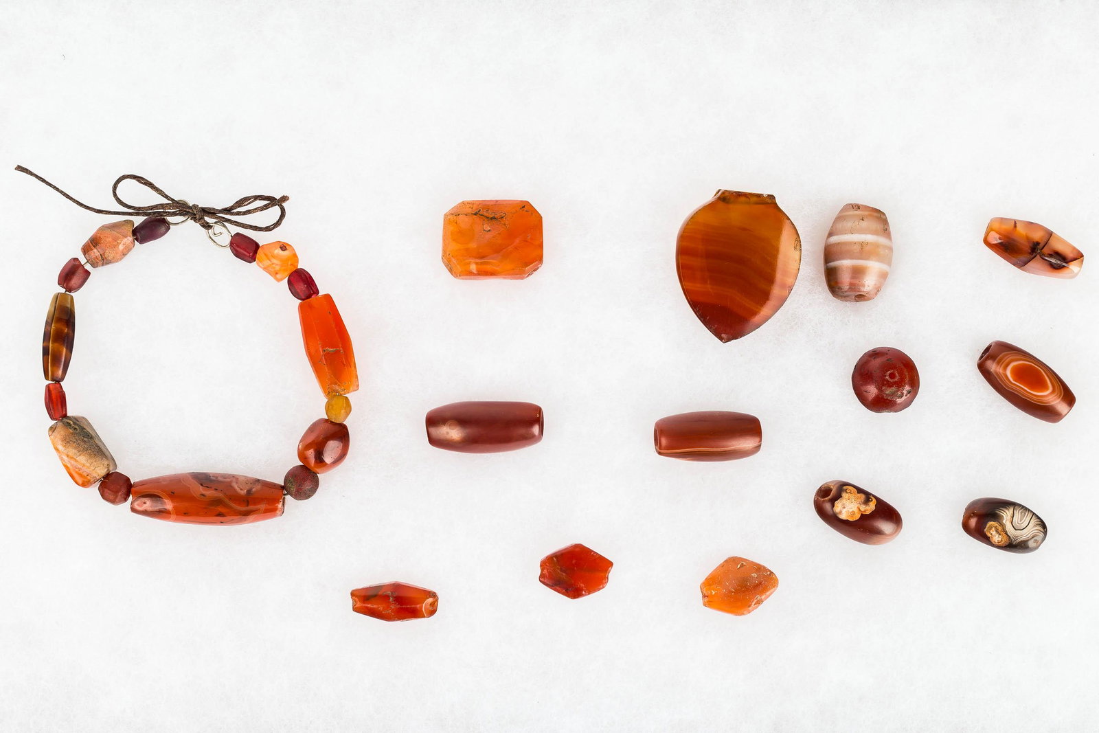 Post-Neolithic Carnelian Biconically Drilled Beads: These beads are from the Sahara in North Africa, from the post-Neolithic period. They are all carnelian, and include a restrung bracelet and (13) loose beads. The largest measures approx. 1.5" L.