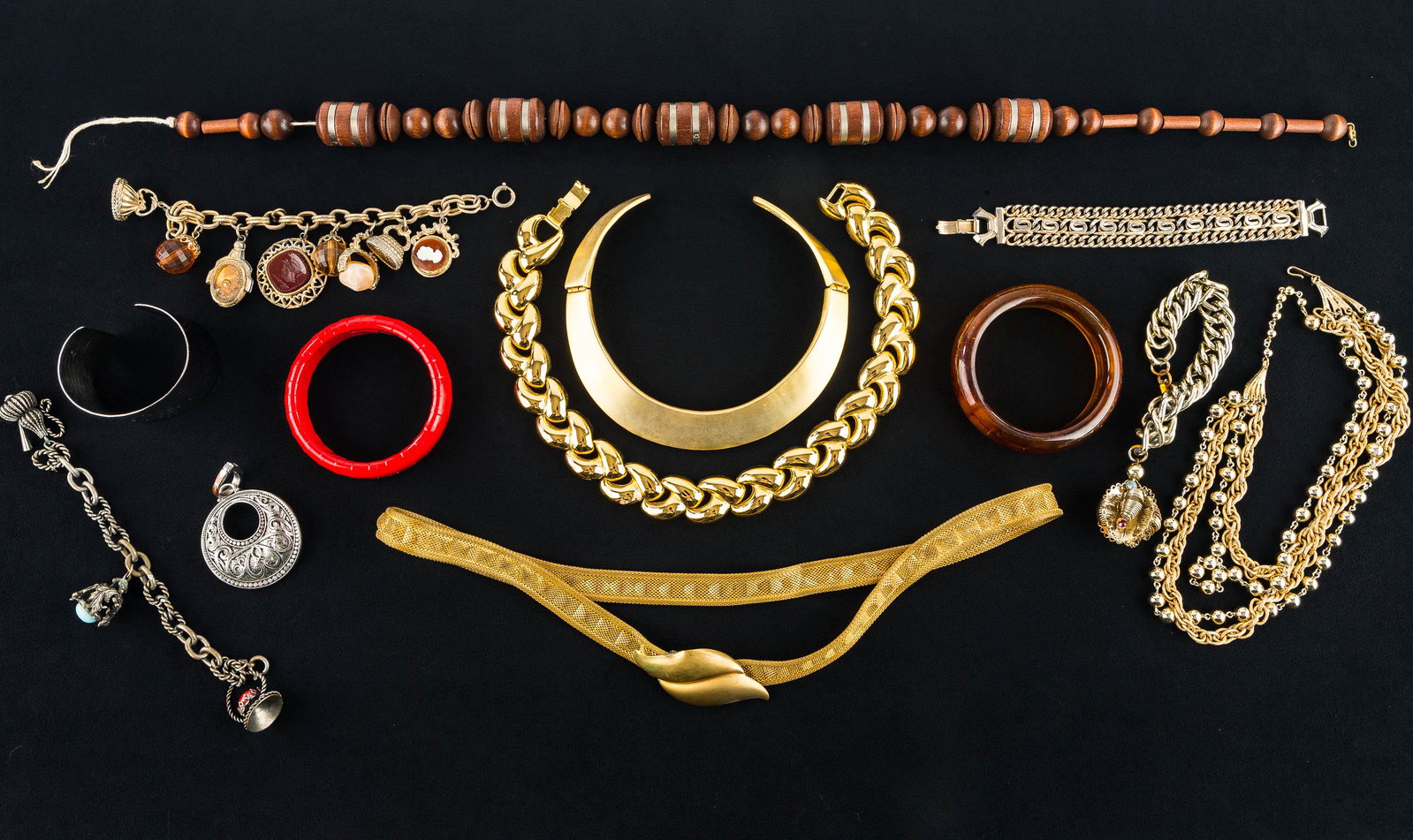Statement Jewelry Collection (2 Trays): This collection features a Forstner gold tone mesh belt measuring approx. 30", a gold tone hinged choker, a heavy gold tone knotted necklace, a stamp charm bracelet. and other statement jewelry.