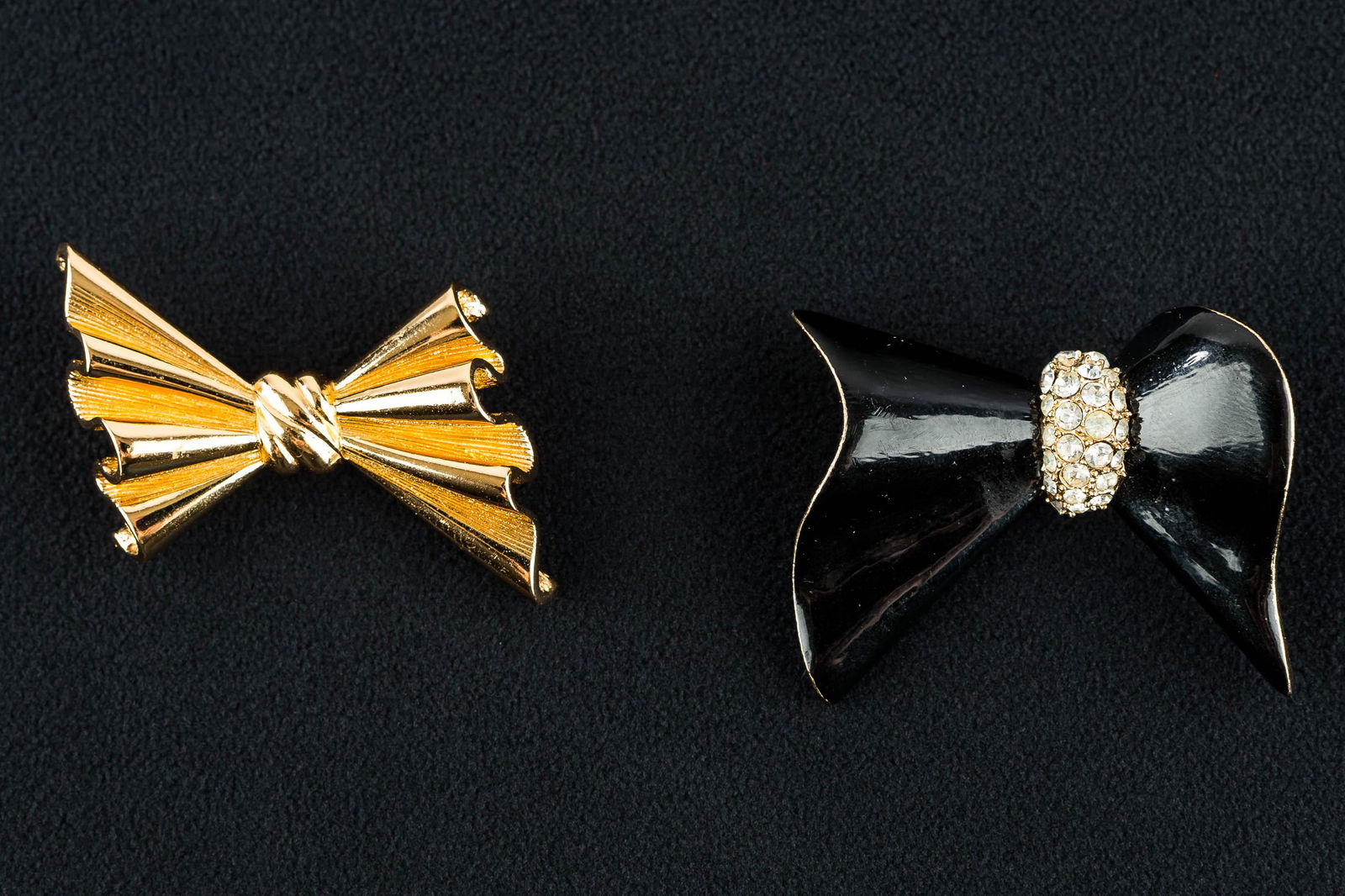 Dior & Ciner Designer Bowtie Brooches: In this vintage lot, a gold tone Dior bowtie brooch measuring approx. 1.75" is accompanied by a black enameled Ciner bowtie brooch (missing two clear rhinestones) measuring approx. 2".