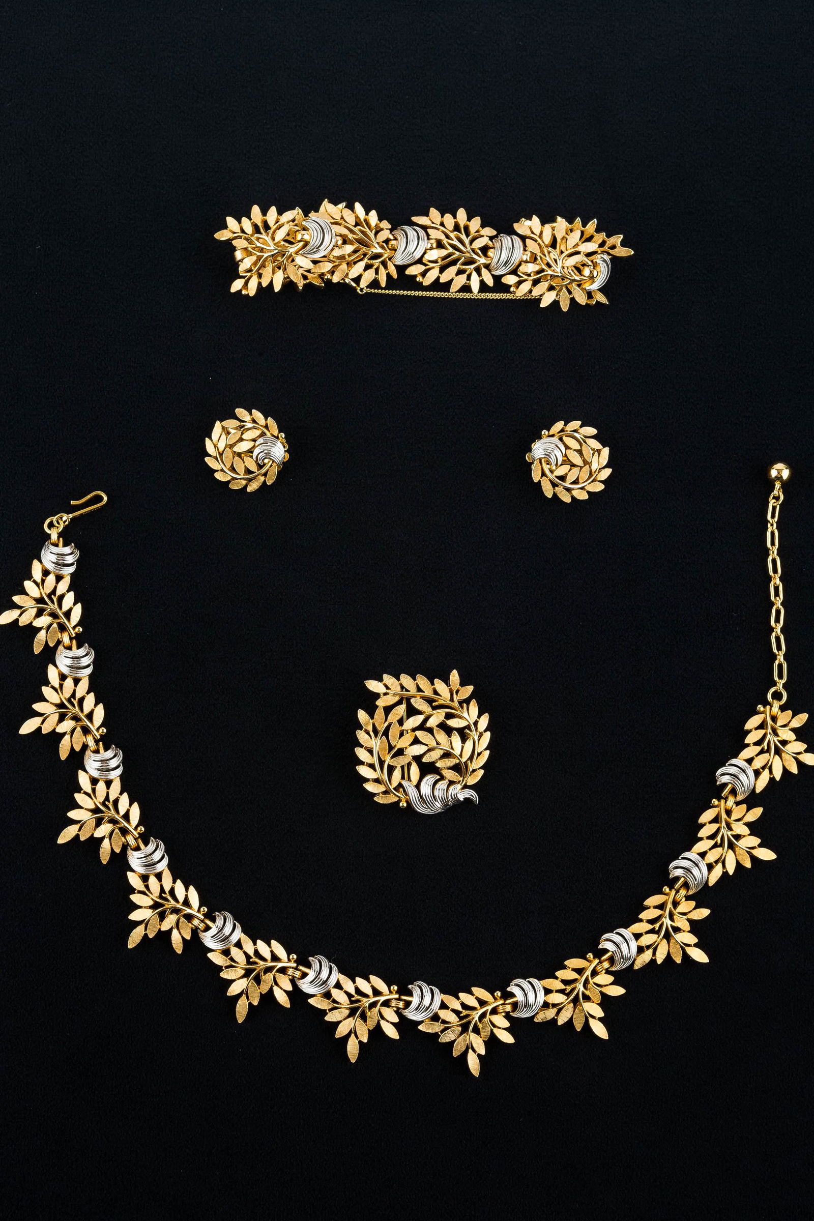 Trifari Vintage Jewelry Suite: This gold tone signed Trifari suite has a crown leaf design with silver accent and includes a necklace measuring approx. 16"L, wide bracelet retaining safety chain measuring approx. 7"L (closed), broo