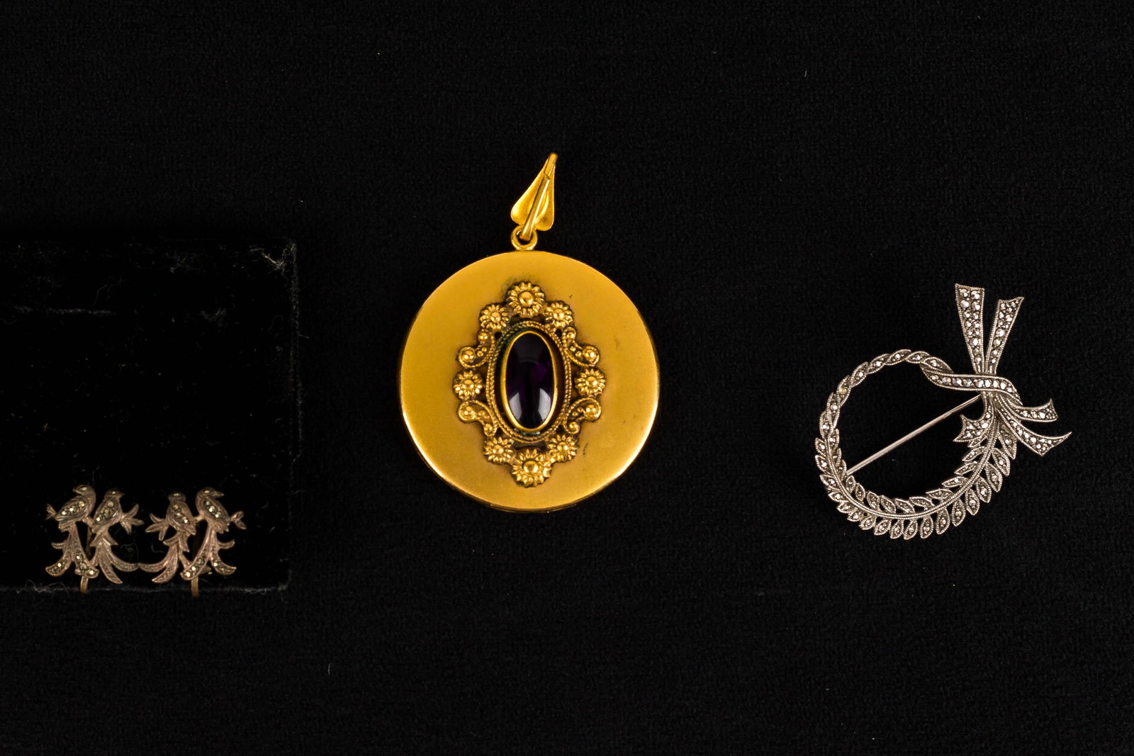 Late 19th/Early20th C Jewelry Collection: This large Victorian locket with a central purple stone measures approx. 1.75" diameter, and is accompanied by a silver and marcasite wreath brooch marked "H6N Silver" and a pair of similar silver lov