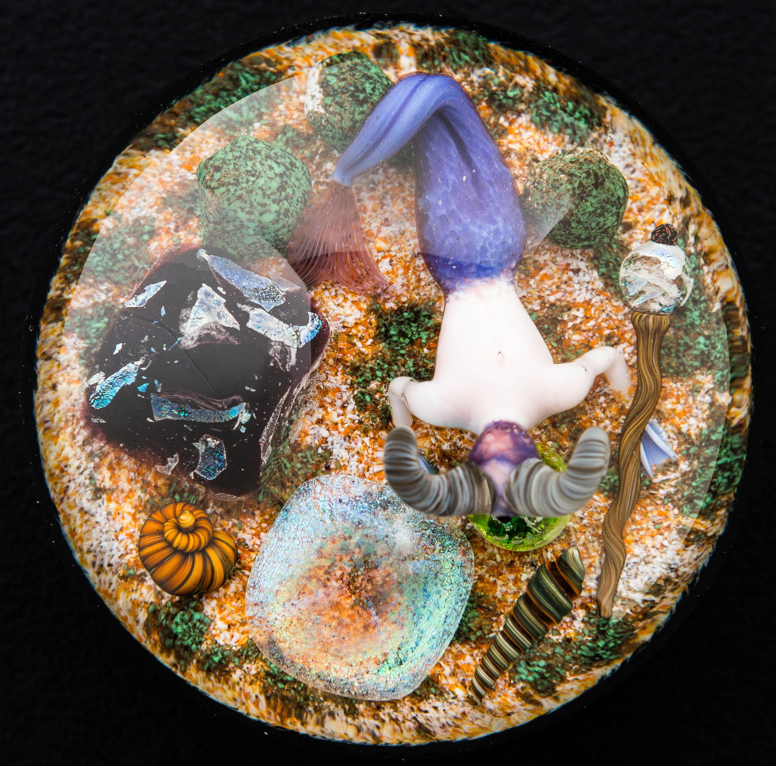 Gordon Smith (American, b.1959) Merman Paperweight: This exquisite lampwork art glass paperweight by Gordon Smith has a merman with a scepter, seashells, and other items. It measures approx. 3" diameter and is hand-etched "GS 99-16." There are no visib