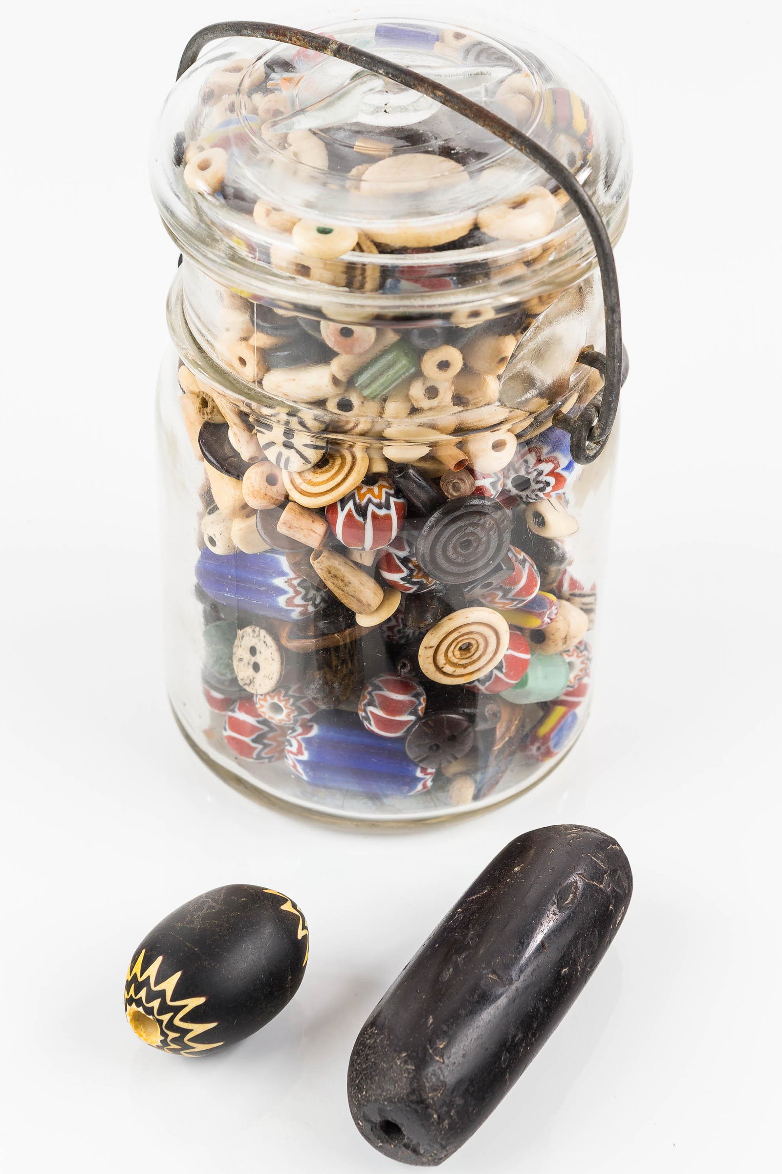 Trade Bead Collection / Variety: There is a black hematite bead 2.75" L, large black Chevron bead 1.25" L, and a jar of mixed beads including glass chevrons, glass cane beads, bone beads, and buffalo tooth beads.
