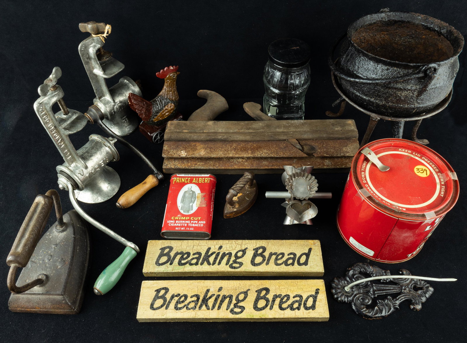 Antique and Antique Style Kitchenware: There is a sad iron, miniature sad iron, molding plane (with oxidation), two meat grinders one by Regal and one by Keystone), tobacco tins, cast iron hook, a 19th century trivet, wood stove shaped ban
