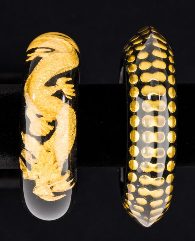 Two Unique Lucite Bracelets: Two large lucite bangles depicting golden encircling dragon and dot designs.
