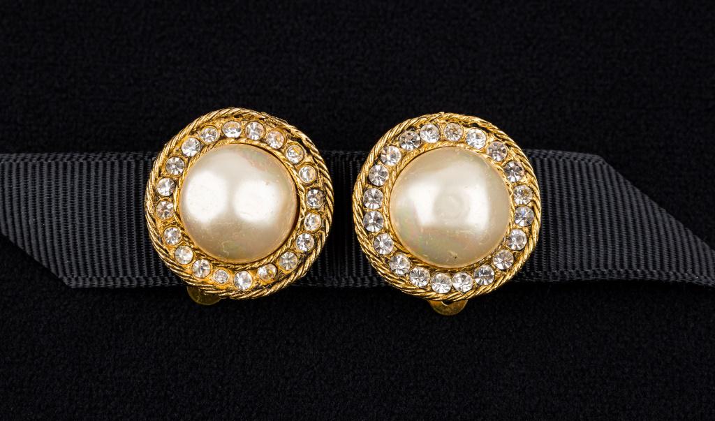 1982 Chanel Clip Back Earrings: Chanel 7/8 diameter clip back earrings with a center 9/16" faux pearl surrounded with 20 rhinestones in gold tone. One earring marked Chanel with CC logo on back with date 1982. The other earring mark