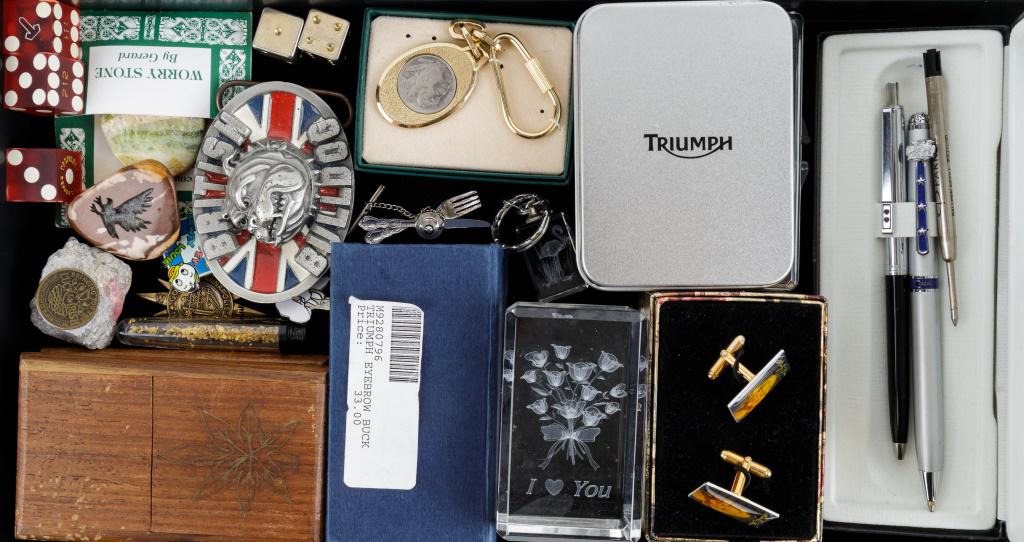 Men's Collectible Dresser Items: British bulldogs belt buckle, multiple sets of dice, a worry stone, Alaskan gold flecks in solution, two Indian card cases, 3 D image of roses in paperweight and Triumph motorcycle keychain and anothe