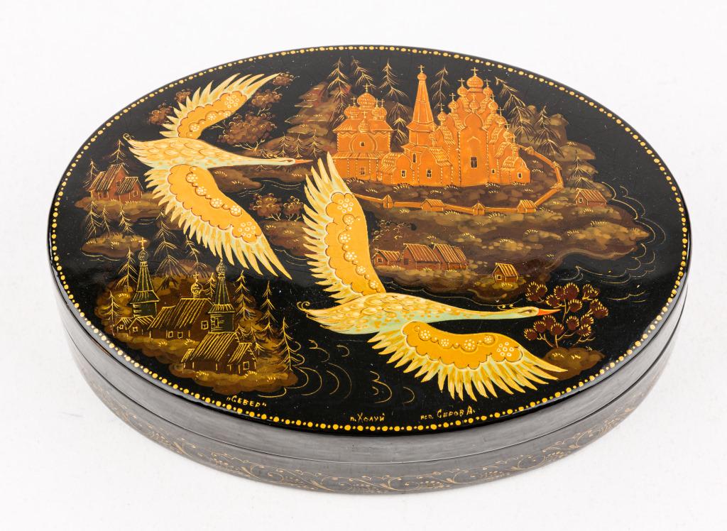 Kholui Russian Lacquer Boxes: Signed Kholui Village Russian lacquer lidded box titled 'Swans Flying North', with insert identifying art school and artist, approx 5.25"L, slight crazing to picture.