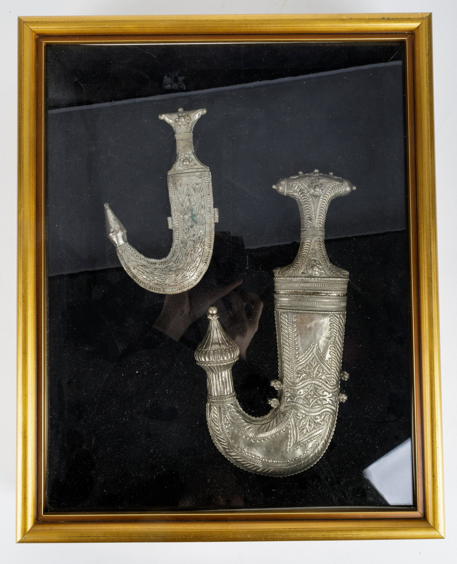 Jambiyas in Glass Case: In glass front case. Larger 10.5 inches, smaller 6.5 inches. Larger Jambiya had dents to sheath. Case is sealed, blade condition unknown.