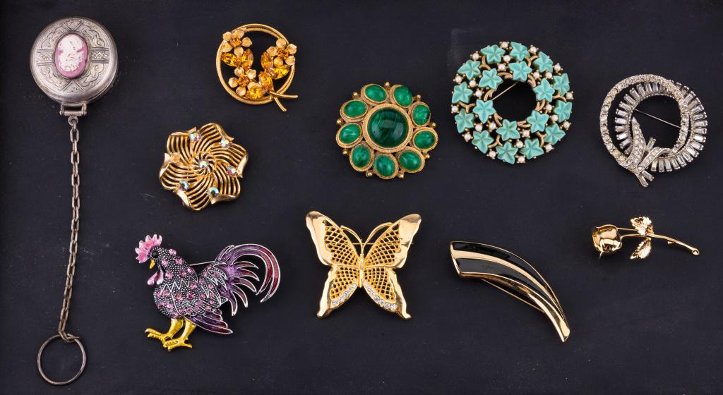 Weiss, Trifari, Lisner & More Costume Jewelry: Lot of 10 pieces of jewelry including a hanging powder box and brooches including Monet rose, teal Crown Trifari circular, Weiss green circular, Lisner with mystic topaz style rhinestones, Trifari bla