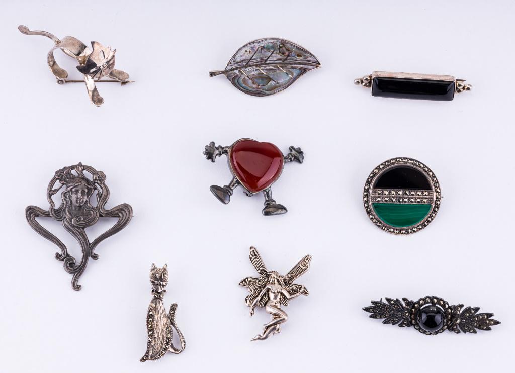 Semi Precious & Sterling Silver Brooches: Lot of nine sterling silver brooches including bar pin with onyx, carnelian heart person and a circular brooch with emerald and onyx, leaf signed Mexico, 3D cat brooch, fairy and more.