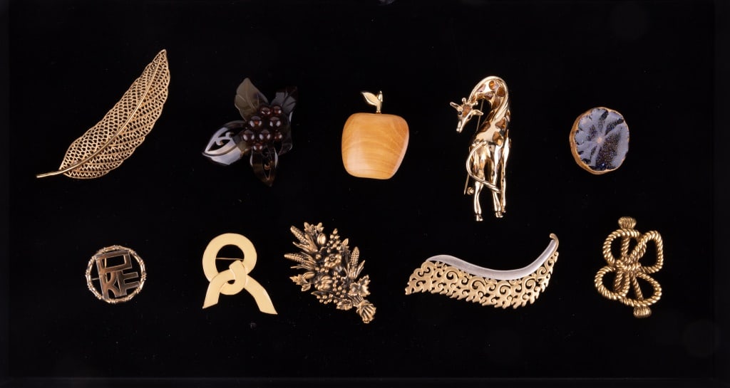 Monet, MMA, Ann Hand & Other Costume Brooches: Lot of 10 brooches including Monet leaf, Ann Hand support ribbon, MAD flower bouquet, MMA USA leaf style, MMA BNM USA knotted bow, FO giraffe, and an apple that is signed and with "Canada". There is a