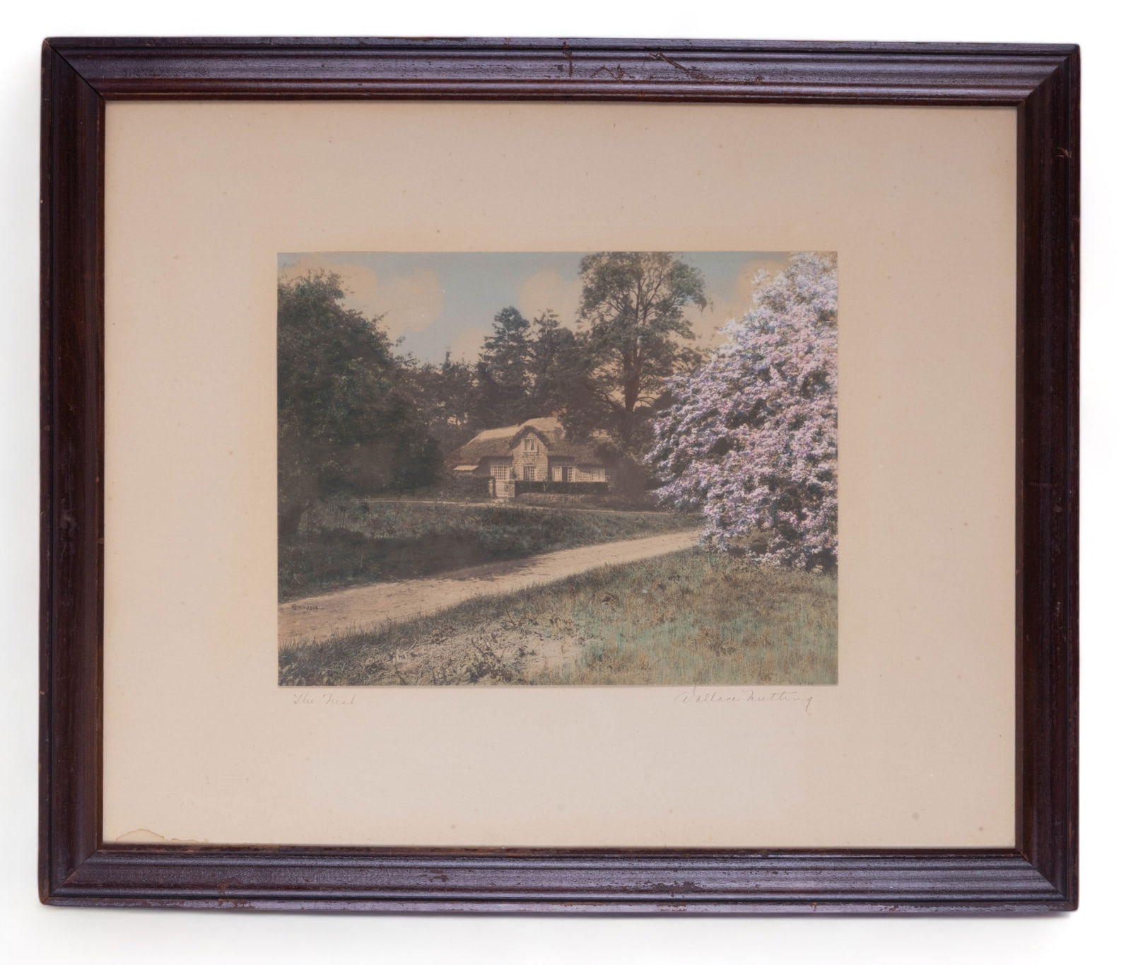 W. Nutting Signed Hand Tinted Photograph: Wallace Nutting (American, 1861 - 1941) signed large framed hand tinted photograph titled "The Nest" of a landscape with cottage in England. Measures approx 18.5" x 22.5" without frame and approx 20.5