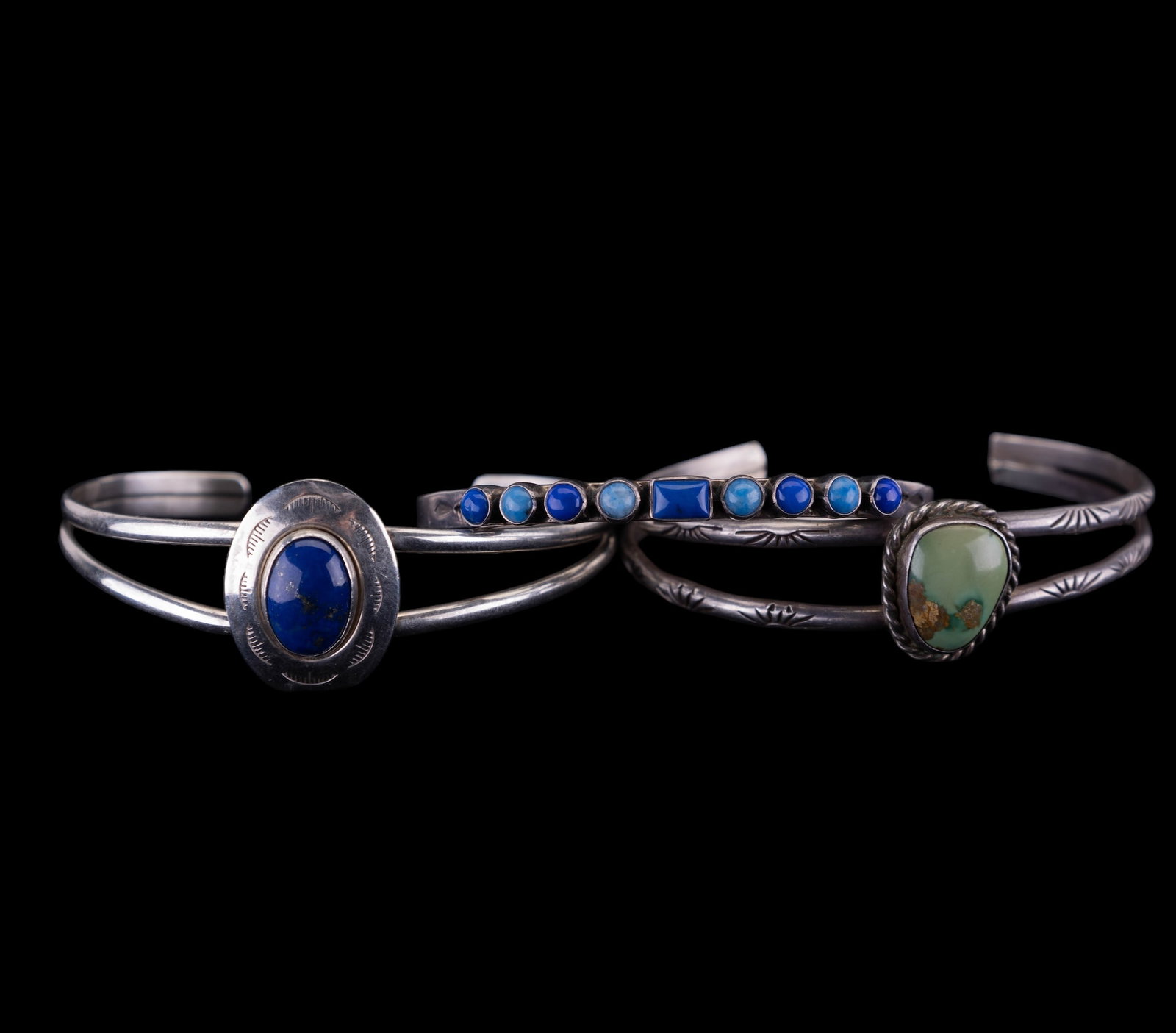 Three Native American Bracelets: Three Native American bracelets featuring a sterling 3/16" finely crafted single band bracelet set with 5 pieces of lapis and 4 pieces of a lighter blue stone; a sterling and lapis split style band br
