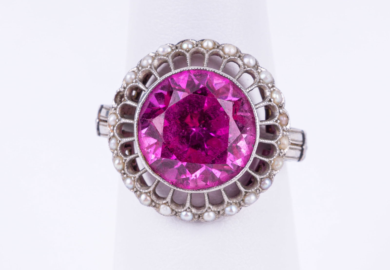 Pink Gemstone and Seed Pearl Ring: Pink gemstone like sapphire in older setting with unclear but presumed platinum hallmark and delicate seed pearl surround. One seed pearl missing. Approx 5.5 grams and ring size 7.