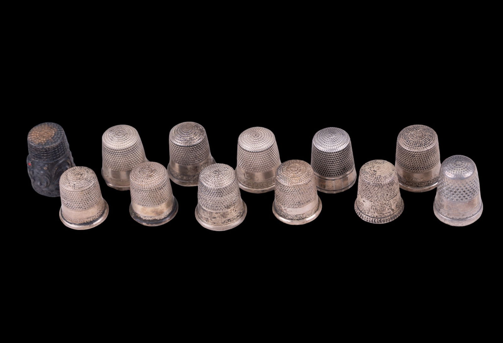 Sterling Silver Thimbles (12): Twelve sterling silver thimbles, some with patterning and engraving on outside, especially near base of thimbles. One thimble has a red eyed owl with relief. Total weight of grouping is approx. 33.2 g