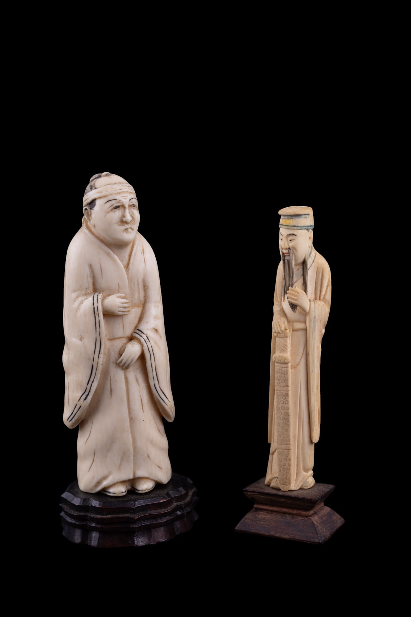 Asian Sage & Robed Man Carved Figurines: Carved bone/natural material sage figure w/ some coloration on his hat, holding a sword. Figure is approx 4.625" tall. Other carved bone/natural material figurine is a robed man w/ a sad or stern expr