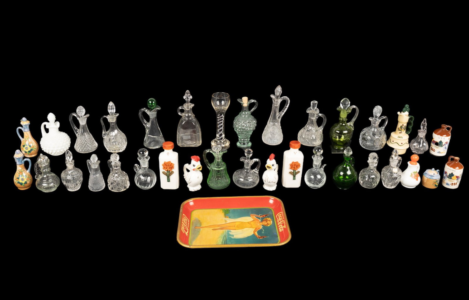 Ceramic & Glass Cruets (31 Pcs) + Glass & Tray: 8 ceramic cruets plus a sugar bowl (6 are vinegar & oil pairs), 22 glass cruets (4 colored, 1 milk glass, many cut glass), a blue twist wine glass approx. 7.75" tall, & a tin Coca-Cola serving tray.