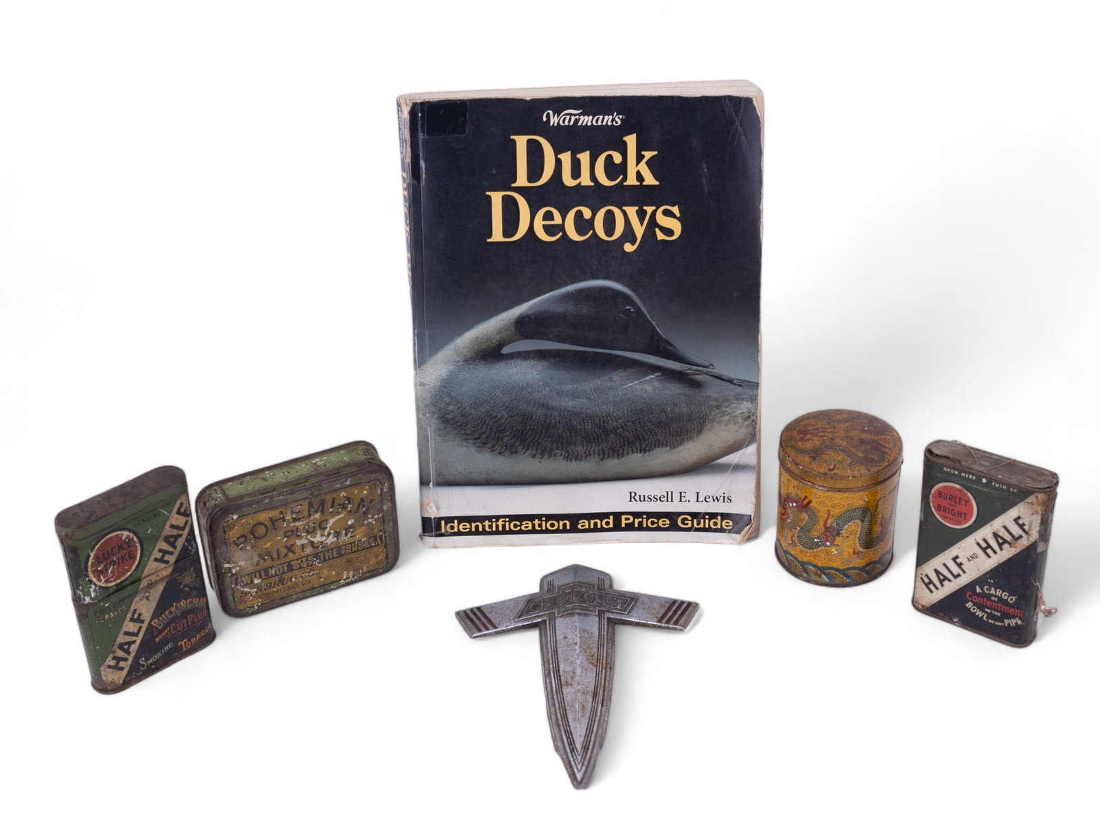 Antique Tins & Emblem & Decoy Guide: Antique Chevrolet hood ornament w/ tip damage (marked 14290), three tobacco tins (Burley & Bright, Lucky Strike, Bohemian Plug Mixture), dragon black tea tin w/ contents, Warman's Duck Decoys price gu