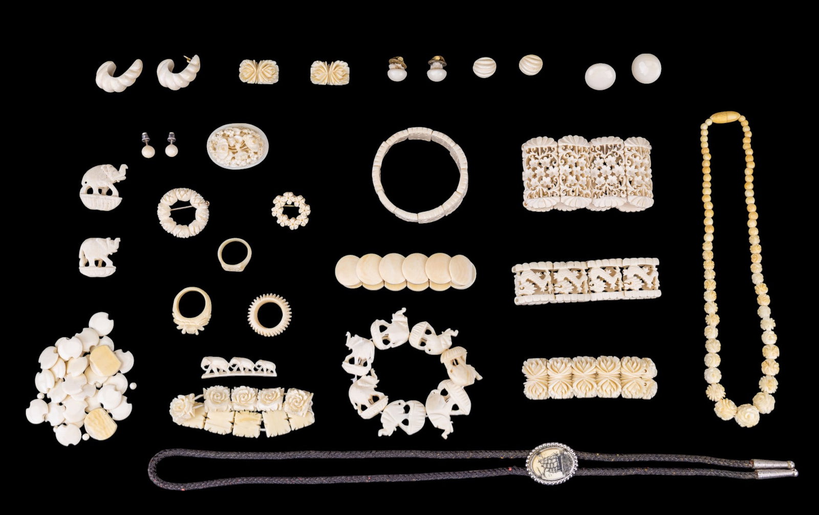 Scrimshaw And Natural Material Jewelry: A collection of 7 carved natural material panel bracelets, natural carved rose bead necklace 14", four carved small brooches, scrimshaw bolo tie, and an assortment of replecement pieces and earrings i