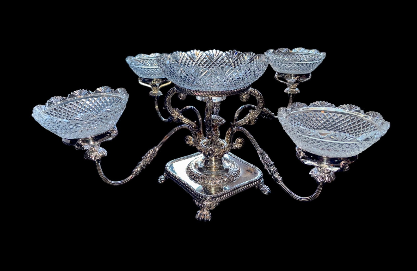 Epergne Silver Plate with Cut Crystal Vessels: Victorian silver plate & cut glass Epergne centerpiece & 2 smaller vessels. Centerpiece measures approx. 10.5" tall & 24" in diameter. All cut glass appears to be perfectly intact. Arms of centerpiece