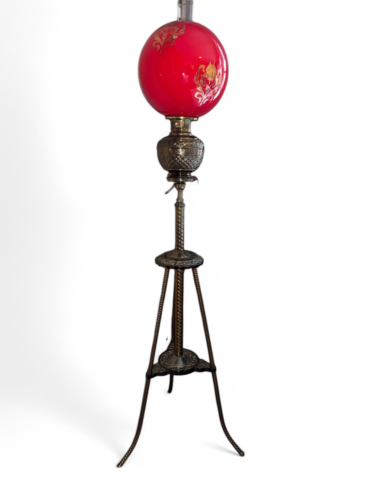 Victorian Tri-Foot Brass Floor Lamp: Gilded Victorian tri-foot brass floor lamp approx 60" to top of chimney. Lamp is highly accented throughout w/ barley twist-type footing & stem & cherry red globe shade w/ gilded floral decoration. Ma