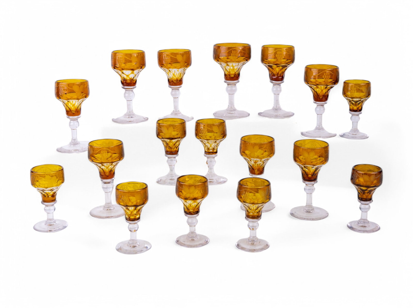 Amber-Colored Cut To Clear Cordials: 2 sets of 8 amber-colored cut to clear glass cordials w/ grape vine motif. Larger set is approx. 4.5" tall.